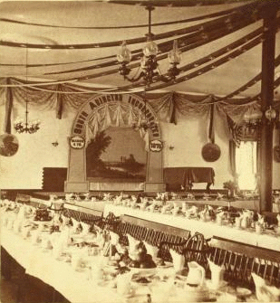 [View of a banquet set in honor of the incorporation of South Abington, tables set, room decorated with streamers.] 1860?-1880?