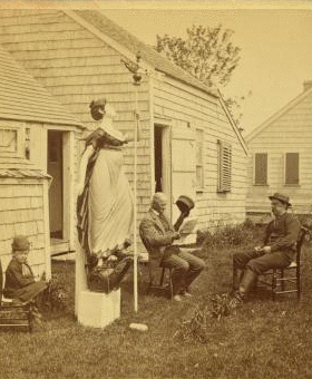 [View of men and a child in a yard with a wood carving of a woman holding a pole topped with a weathervane.] 1867?-1890?