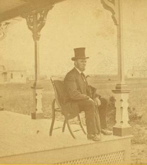 [View of a man with a beard and top hat on a porch.] 1868?-1880?