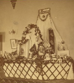 [Interior view of a fair or church bazaar showing tables draped with flowers and arranged with items, including a table with photographs and paintings labelled "In Memoriam".] 1865?-1900? [ca. 1880]