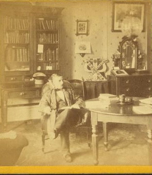 [Young man wearing jacket made of ornate material sitting in the Chi Psi fraternity room at Amherst College.] 1869?-1880?