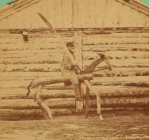 "Punishment Horse Bridger" [showing soldier on wooden horse holding oversized wooden sword over his shoulder in front of log building]. 1865?-1897