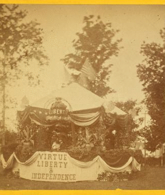 [Decorated tent [Fourth of July?], with American flags, ornamental plants, liberty bell in flowers, and drapery bearing phrase 'Virtue Liberty & Independence;' bearded, hatted man stands inside.] 1860?-1915?