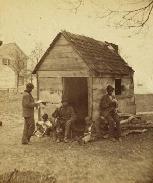 Uncle Abe's schoolhouse and scholars. [Man in a top hat in front of a shack with several boys with books.] 1868?-1900?