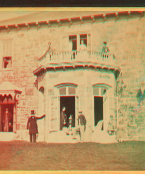 [Family posing in front and in the balcony of stone house.] 1860?-1869?