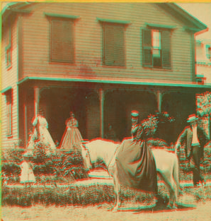 [Miss Olive Jones sitting sidesaddle on her horse as others look on from the porch of a home.] 1865?-1885?