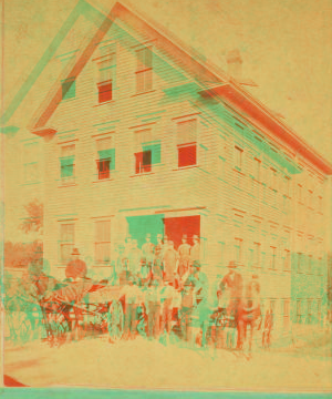 [Men in front of four story clapboard building with wagons.] 1865?-1885?