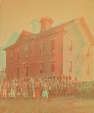 [View of unidentified students and teachers in front of wood frame school.] 1870?-1880?