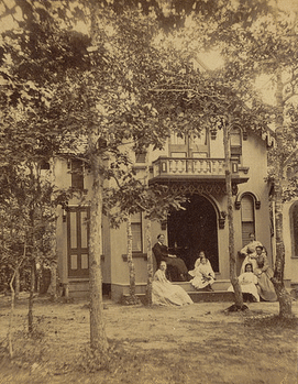Four women and three girls seated by the entrance of their cottage on Martha's Vineyard