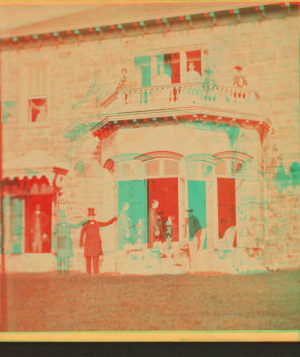 [Family posing in front and in the balcony of stone house.] 1860?-1869?