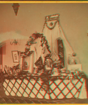 [Interior view of a fair or church bazaar showing tables draped with flowers and arranged with items, including a table with photographs and paintings labelled "In Memoriam".] 1865?-1900? [ca. 1880]