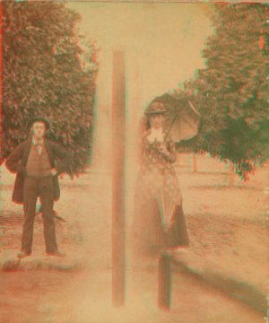 [Man and woman, with parasol, standing behind double fountain.] [ca. 1880] 1870?-1910?