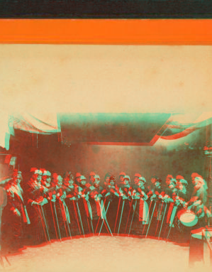 [Studio view of a group of women holding brooms(?) and 1 woman with a drum.] 1865?-1885?