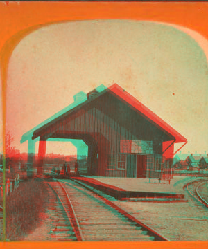 [View of railroad depot with shed roof over tracks.] 1865?-1880?