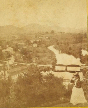 [View of a woman looking into the distance with binoculars above Glendale, showing a bridge, a mill, and homes below.] 1865?-1905?