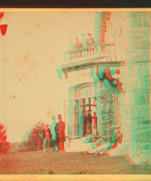 [Family posing in front and in the balcony of stone house.] 1860?-1869?