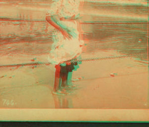 [Young woman wading at the beach, in front of a covered pier.] 1868?-1900?