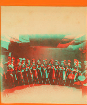 [Studio view of a group of women holding brooms(?) and 1 woman with a drum.] 1865?-1885?