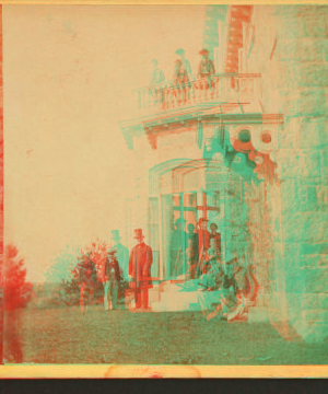 [Family posing in front and in the balcony of stone house.] 1860?-1869?