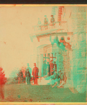 [Family posing in front and in the balcony of stone house.] 1860?-1869?