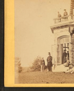 [Family posing in front and in the balcony of stone house.] 1860?-1869?