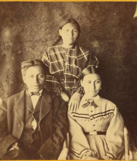 [Portrait of two young women and one young man, animal skin used as backdrop.] 1870?-1880?