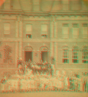 [Boys and girls pose with adults on front steps of large brick institutional building.] 1860?-1900?