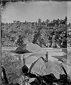 Green River. Red Canyon, Ashley Falls, portage of boats. Beaman photo, 1871. This photo shows two men with rope and another one below possibly with rope portaging the boat through the falls (the lower man does not show clearly due to spray from the falls)