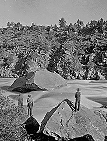 Green River. Red Canyon, Ashley Falls, portage of boats. Beaman photo, 1871. This photo shows two men with rope and another one below possibly with rope portaging the boat through the falls (the lower man does not show clearly due to spray from the falls)