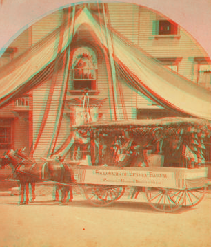 [Decorated wagon with women riding in it, banner on side reads "followers of Betsy Baker preparing and braiding domestic straw," in front of building with bunting.] 1865?-1880?